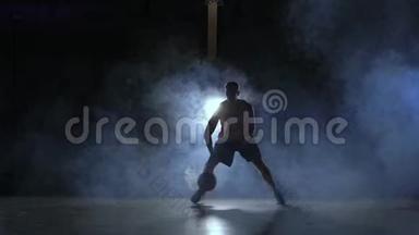 一个男子在黑暗的篮球场上打篮球，背景是烟雾中的篮球戒指